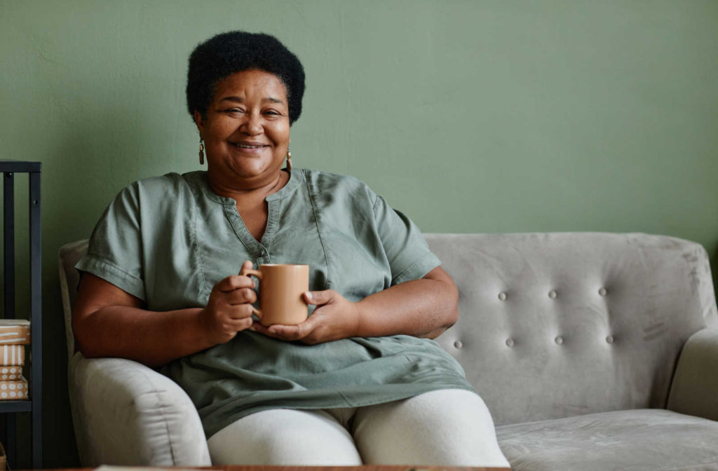 Happy senior woman enjoying a cup of coffee on her couch at an assisted living facility.