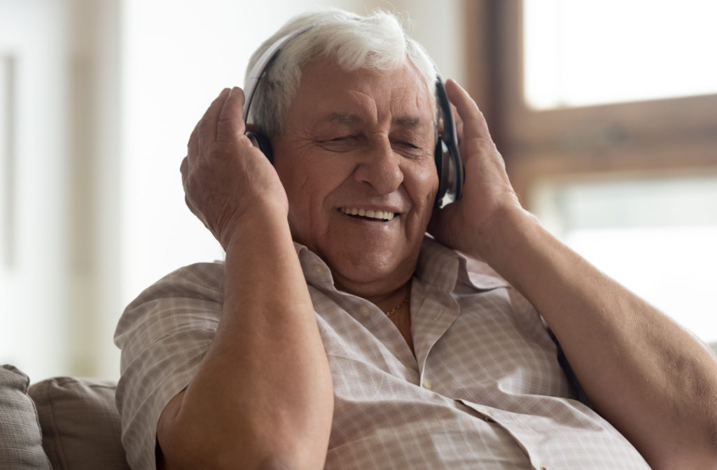 A senior man sitting on a couch wearing headphones and listening to music