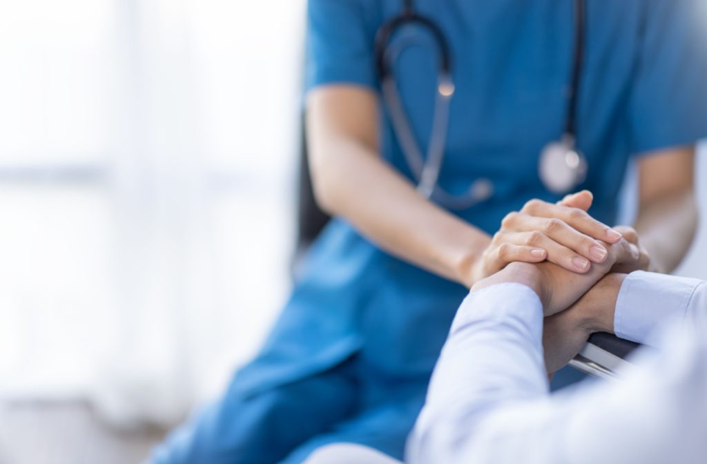 A close up image of a nurse holding a senior's hands in a well lit room. 