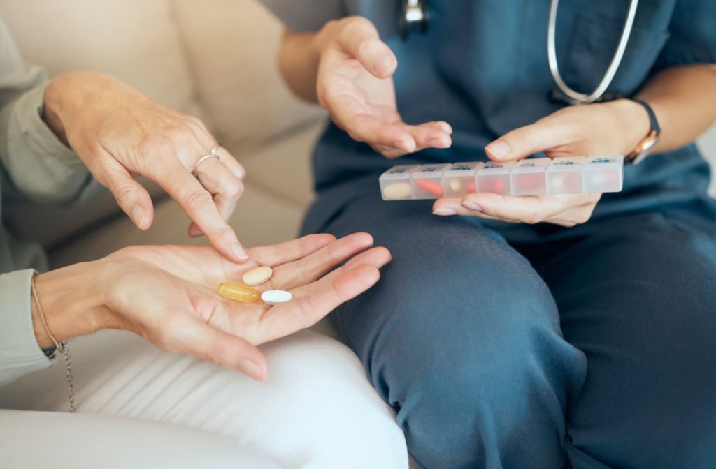 A nurse holding a pill organizer and a senior pointing to pills in their hands sit on a couch together as the nurse teaches medication safety.