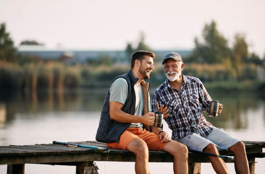 A happy man and his older adult father with demential having a conversation by the pier.