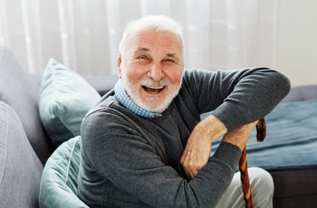 An independent older adult in assisted living sitting on the couch and smiling at the camera.