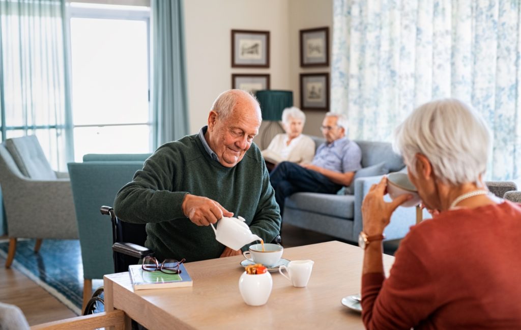 Two seniors sit and have tea at a table in the bright, welcoming dining room in their assisted living community.