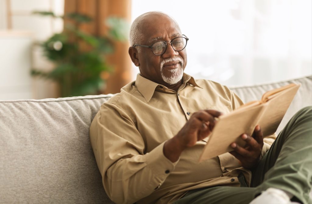 Older man reading a book, sitting comfortably on a couch, smiling and enjoying his leisure time.