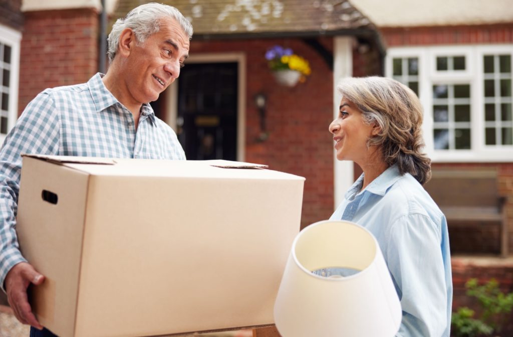 A mature couple exchanges knowing glances, their hands gripping boxes filled with treasured belongings and furniture, as they prepare to downsize for their move to assisted living.