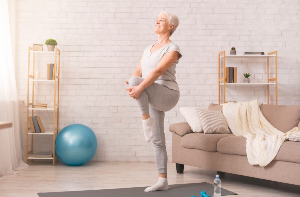 An older adult in their living room doing a standing leg raise to loosen tight hips.