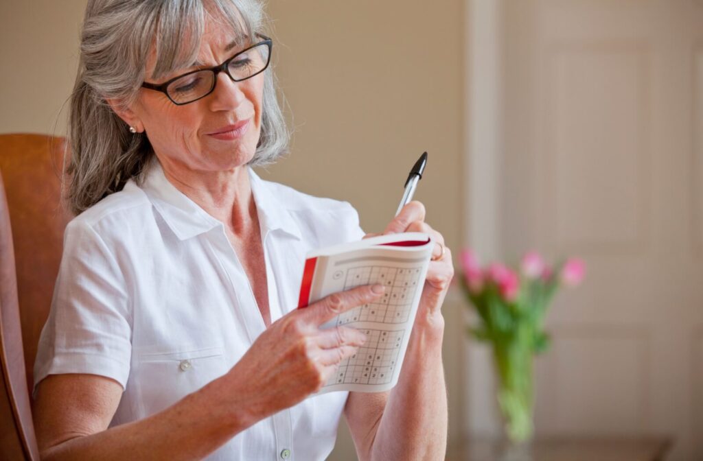 A senior relaxes in a chair by completing a sudoku puzzle, working to improve their cognitive abilities in memory care