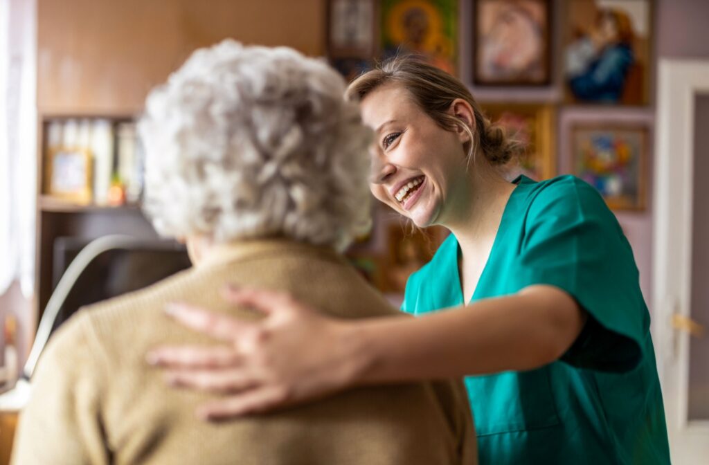 A smiling nurse rests their hand on a senior’s back, happy to help with care needed in memory care