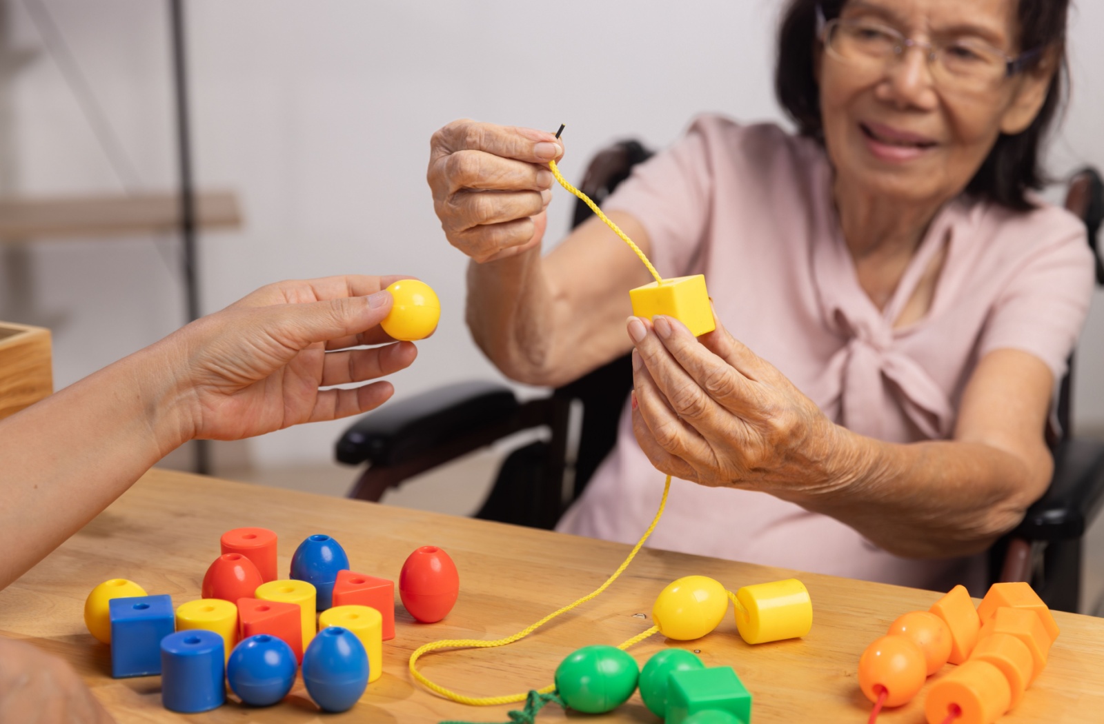 A senior with dementia threads different-sized blocks onto a string as a therapeutic activity offered in memory care