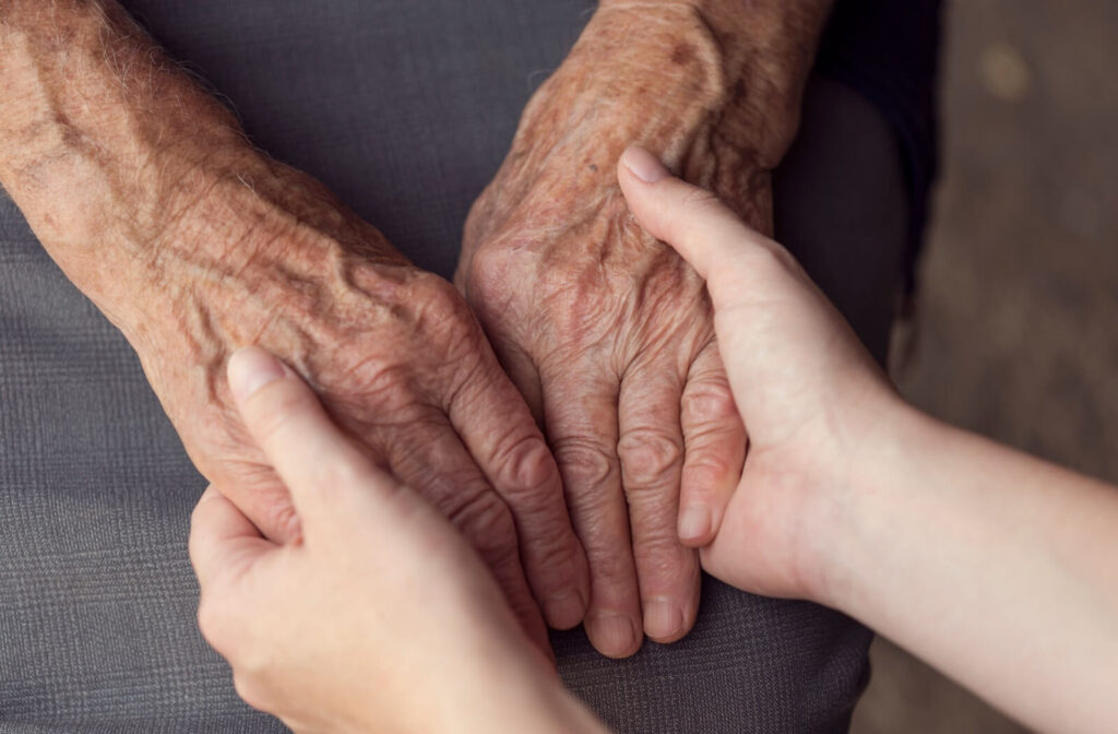 An adult child clasps their older grandparent's hand during a visit to memory care