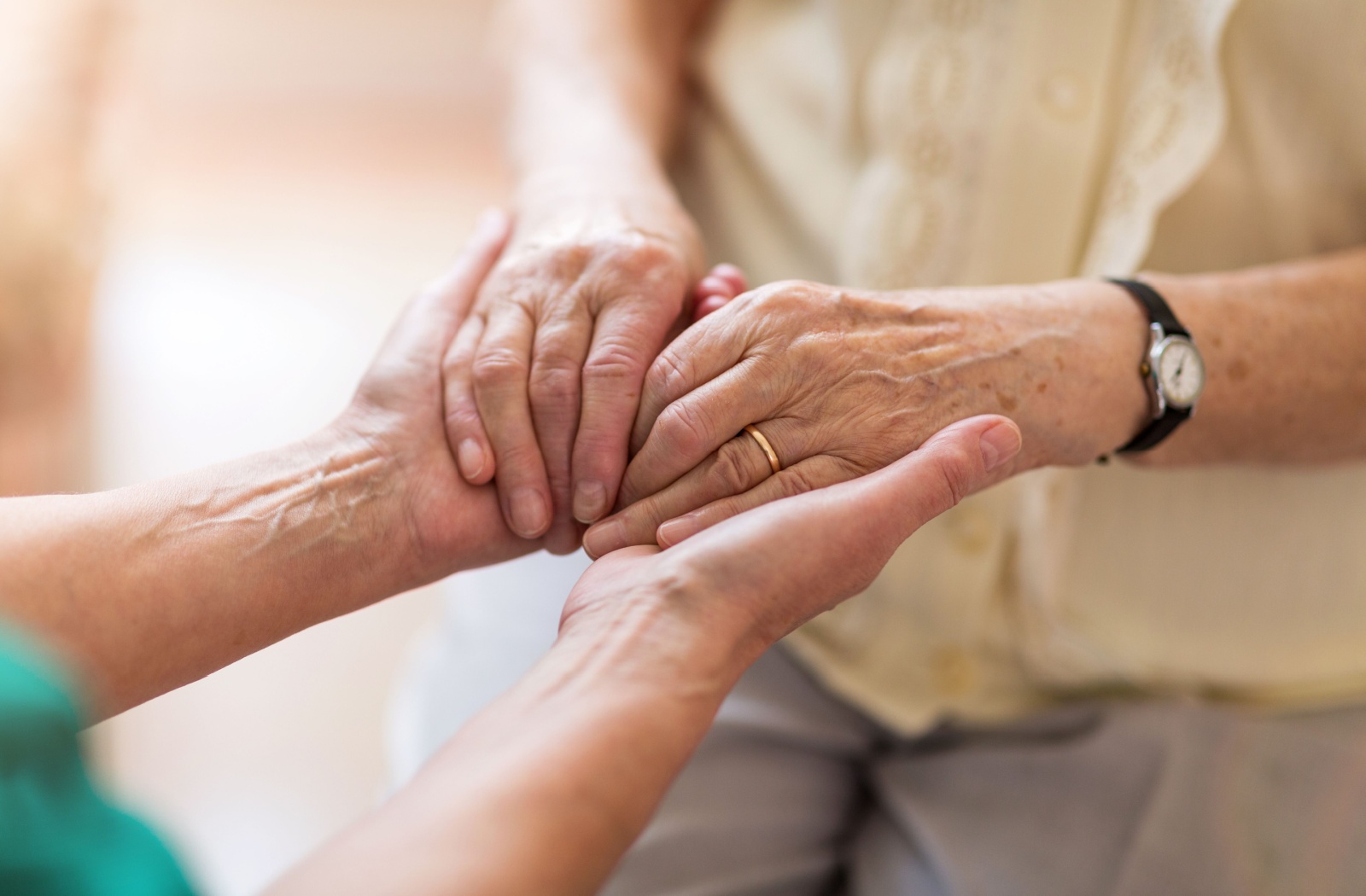 A close-up of an adult child holding their older parent's hands in support talking about their living situation.